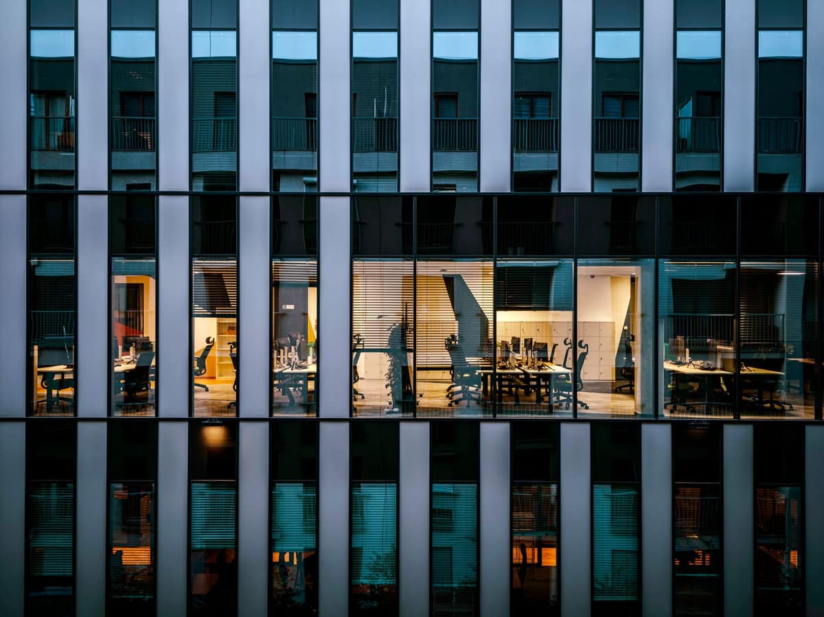 A glass and metal office building lit up at dusk